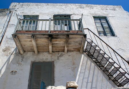 An aged and weather worn balcony balcony at a village house on the island of Anti Paros. In the historic Kastro. The steps leading up to the construction cast shadows over the whitewashed walls.の写真素材
