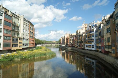Girona, Rio Onyar. Medieval town, summers day. The old town houses by the river reflected in the still waters. Blue sky and nature and city in harmony. Colorful houses on the river bank.の写真素材