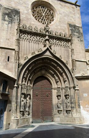 A view of a beautiful, arched doorway at the ancient Murcia cathedral.  Decorative, Gothic, carved arches frame the heavy, medieval old doorの写真素材