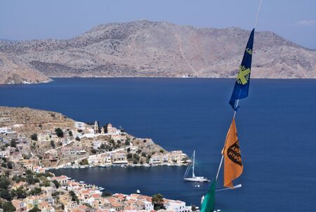 A view from a hillside over the port of Symi, Greece.  Religious, orthodox flags form the foreground with the background mildly blurred.の写真素材