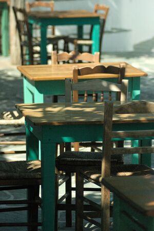 Taverna tables and chairs at a traditional Greek restaurant on the island of Folegandros.  Sunlight...