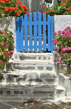 Sikinos island, Greece. Blue gate to a traditional village house. Colorful flowers.  Authentic Greek scenery.  Vertical shot.の写真素材
