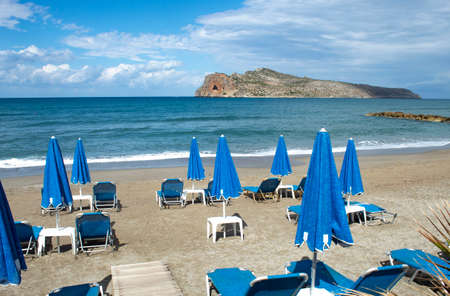 Crete island, Greece Agia Marina beach near Chania Parasols and sun loungers on the sands Rocky outcrop on the horizonの写真素材