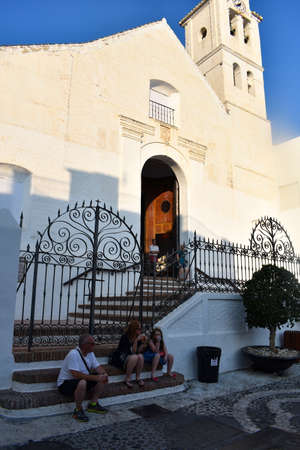 Frigiliana - Spain - August 18 2018 :  Historic old church in the village square  Holiday makers relax in the warm late afternoon by the historic building  Vertical shotのeditorial素材