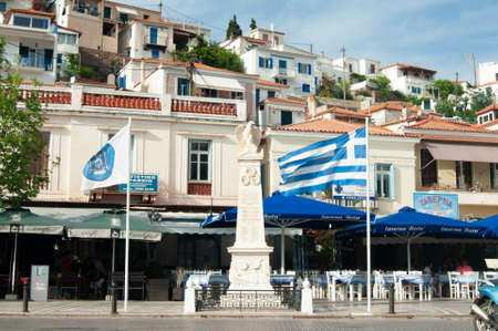 Poros town -  Greece - May 21 2018 : Busy waterfront at the charming old town. View of war memorial, with background of taverna's and bars. Landscape aspect shot.のeditorial素材