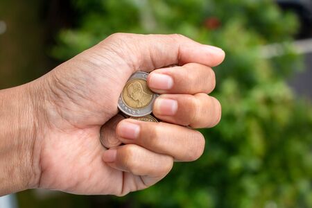 Clutch a coin to save money. The economy was bad during the epidemic. holding the coins on natural background. in saving money concept. copy spaceの写真素材