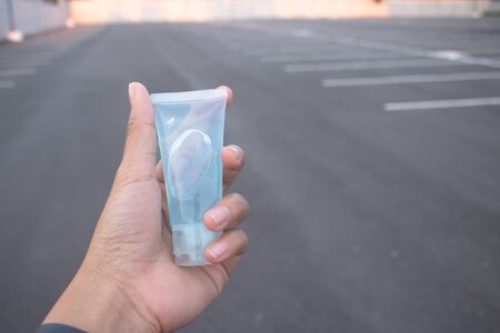 Blue alcohol gel bottle Holding on the hand and the background is a gray road Alcohol gel for hand washing. Anti-virus and anti-bacterial and anti-virus. Covid-19 copying area.の写真素材