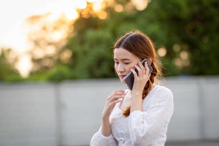 Displeased  and disappointed girl with a mobile phone stands in parking lot . In the evening the sunset was orange. copy space.の写真素材