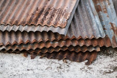 Sharp edges of the rusty metal sheets placed on the floor. Old aged weathered rusty galvanized corrugated iron sheet roof of abandoned mood. selective focus blur background. Vintage.の写真素材