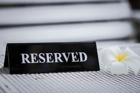 Reserved metal black plate in a restaurant. Reserved metal plate On the white table. vintage photo processing. close up of a setting a reserved sign on the restaurant table.の写真素材