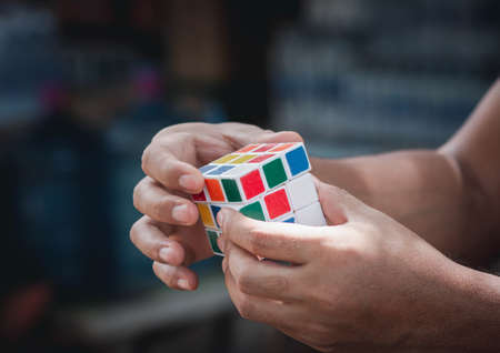 CHON BURI, THAILAND - JULY 29, 2020: Handsome man wearing casual clothes collect Rubik's Cube. Rubik's Cube invented by a Hungarian architect Erno Rubik in 1974. Selective focus. Copy space.のeditorial素材