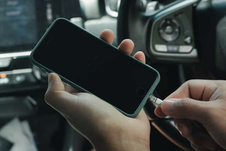 Hands man holding and charging battery mobile smartphone in car with cable in luxury interior car design. The phone is charging from the car.の写真素材