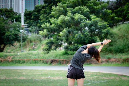 Young woman has an outdoor workout at the park. She is stretching her arms and looking away. Health care,の写真素材