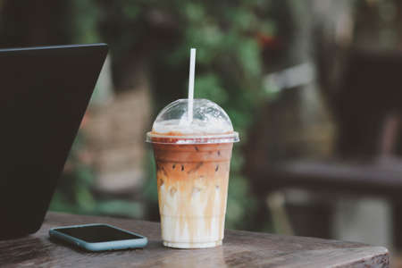 Laptop on wooden desk with iced coffee in the cafe.の写真素材