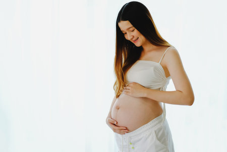 Young beautiful pregnant woman standing of happy pregnant woman with big belly at window. Smiling...