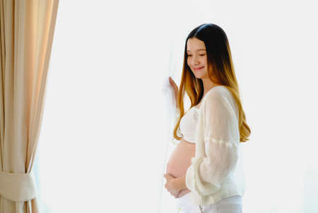 Young beautiful pregnant woman standing of happy pregnant woman with big belly at window. Smiling pregnant woman.の写真素材