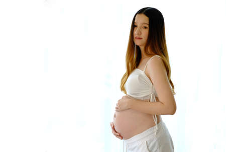 Young beautiful pregnant woman standing of happy pregnant woman with big belly at window. Smiling pregnant woman.の写真素材