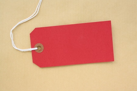 Red paper luggage tag or label with copy space on a brown wrapping paper