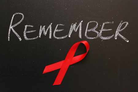 Red Aids awareness ribbon on a blackboard under the word Remember 