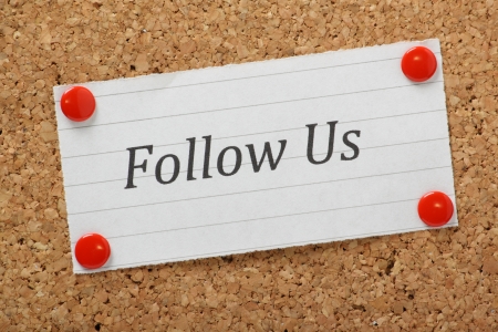 The phrase Follow Us typed on a piece of lined paper and pinned to a cork notice boardの写真素材