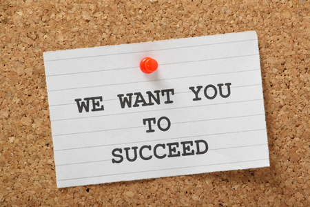 The phrase We Want You to Succeed typed on a piece of lined paper and pinned to a cork notice boardの写真素材