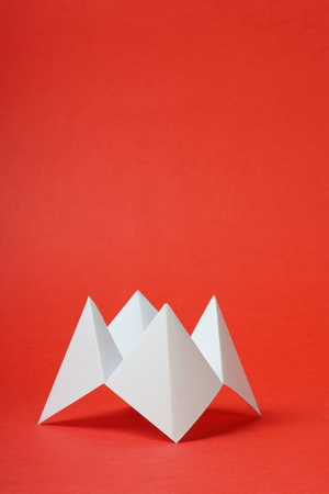 An origami fortune teller or cootie catcher made from blank white paper on a red with room for your text の写真素材
