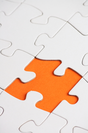 A blank white jigsaw puzzle with one piece missing on orange paper の写真素材