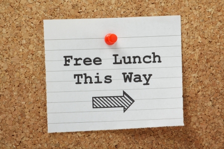 The phrase Free Lunch This Way with a direction arrow typed on a piece of paper and pinned to a cork notice board の写真素材