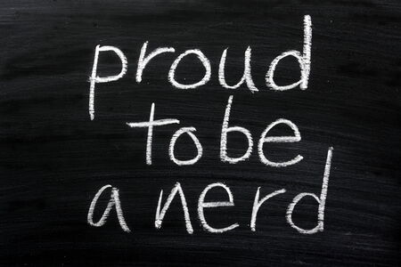 The phrase Proud To Be A Nerd written by hand in white chalk on a used blackboardの写真素材