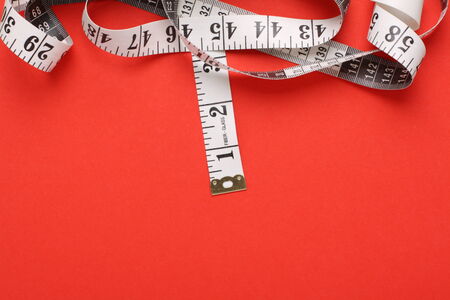 White tape measure with both inches and centimetres on a red paper