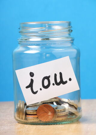 A jam jar part filled with british coins for savings has been slapped with a white sticker that says I O U  the abbreviation for I Owe Youの写真素材