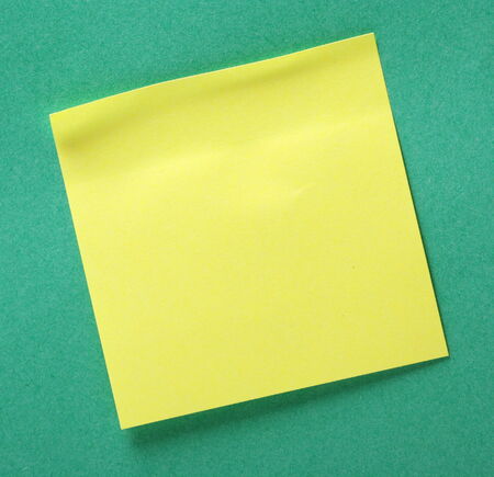 A blank yellow sticky note on a green paper background with copy space