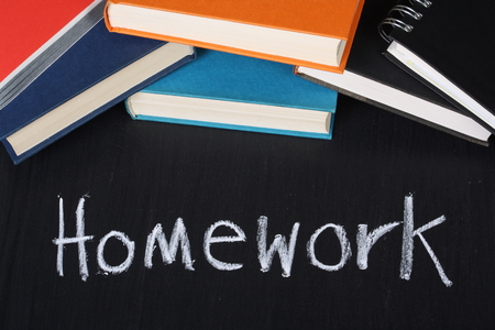 The word Homework written in chalk on a blackboard next to a pile of school booksの写真素材