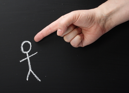 A giant hand pointing the index finger at a chalk stick figure on a blackboardの写真素材