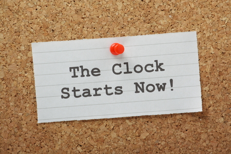 The phrase The Clock Starts Now typed on a piece of lined paper and pinned to a cork notice boardの写真素材