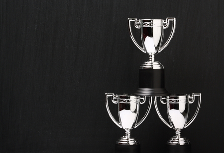 Three miniature silver trophy cups arranged in front of a used blackboard with copy spaceの写真素材