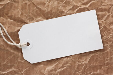 Blank white luggage tag or label with copy space on a background of crumpled parcel paperの写真素材