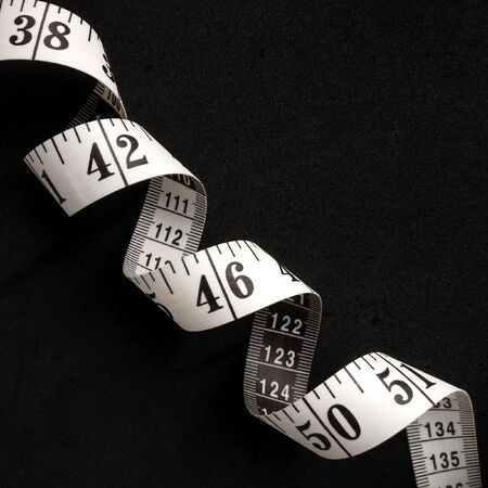 White tape measure with centimeters and inches on display, curled on a black background with copy...