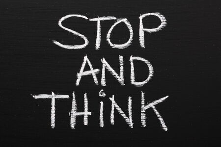 The phrase Stop and Think written on a blackboard as a reminder to take time out and work through our options before taking actionの写真素材