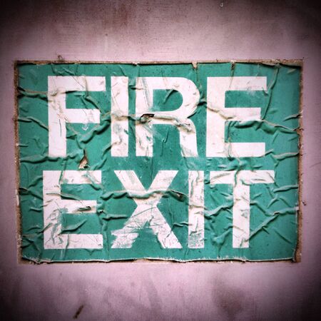 A wrinkled and damaged Fire Exit sign stuck to an outside door. Creative filters and textures have...