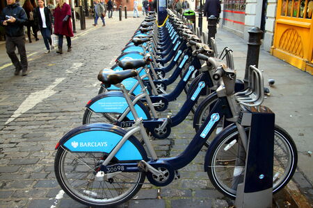 London, England - February 17, 2015: Pedestrians pass by Barclays Bank bicycles parked in a cobblestone street in London, England. The rental scheme provides over 5000 bikes for hire across the city.のeditorial素材