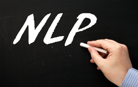 Hand writing the letters NLP on a blackboard with a chalk stick. NLP refers to Neuro Linguistic Programming a method of changing the way we communicate and perform in business and lifeの写真素材