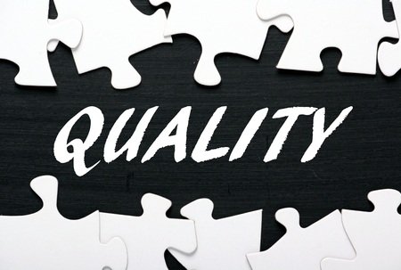 The word Quality in white text on a blackboard with a border of jigsaw puzzle piecesの写真素材
