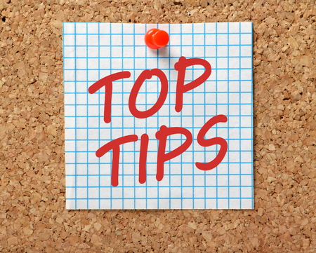 The words Top Tips in red text on a piece of square graph paper pinned to a cork notice board as a reminderの写真素材