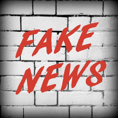 The words Fake News in red text on a white brick wall as a reminder to be aware of hoaxes and disinformation for propaganda usesの写真素材