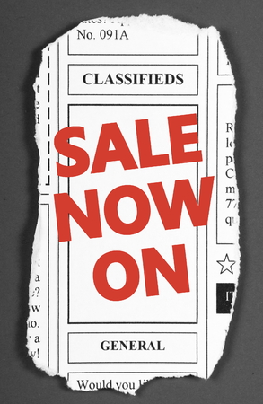The words Sale Now On in red text on a clipping from the classified advertising section of a newspaperの写真素材