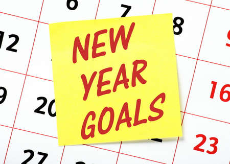 The words New Year Goals in red text on a yellow sticky note posted on the page of a calendar as a reminderの写真素材