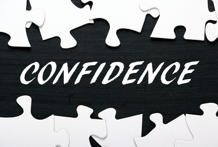 The word Confidence in white text on a blackboard with a border of jigsaw puzzle pieces as a metaphor for unlocking your potentialの写真素材