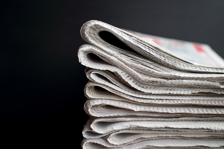 Stack of folded newspapers in front of a black background with copy spaceの写真素材