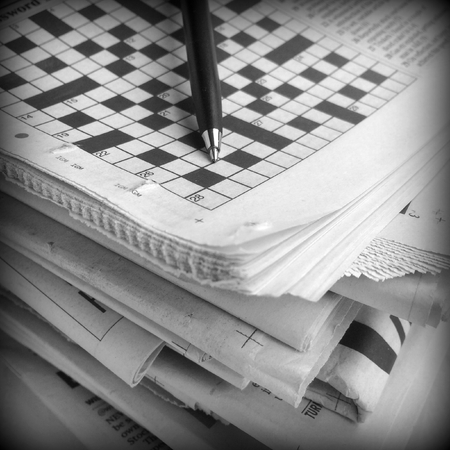 Pen and Crossword Puzzle on top of a stack of newspapers with a shallow depth of field. A vignette has been added for effectの写真素材